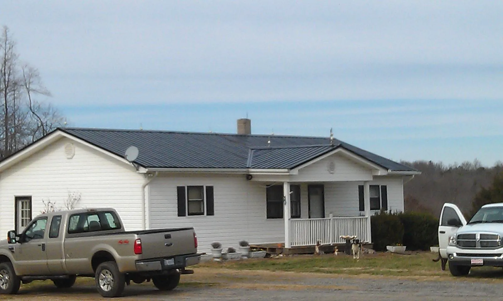 Finished dark metal roof on a white ranch home with work trucks parked in Peru